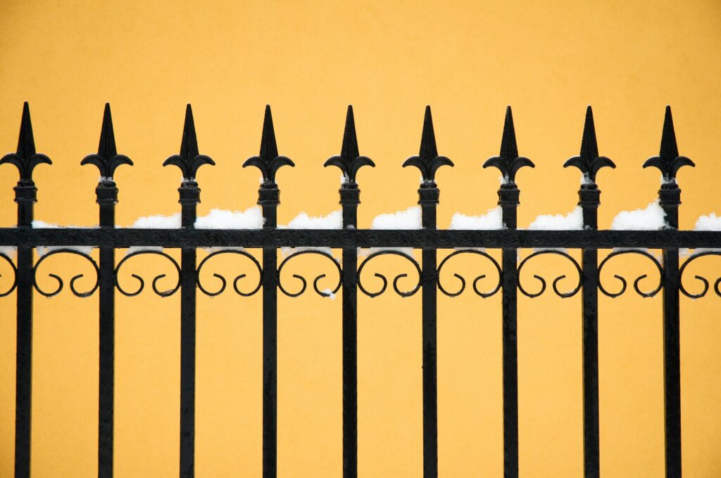 old fashioned spike fence against yellow wall, some snow